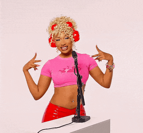 a woman wearing a pink crop top and red headphones is standing in front of a microphone