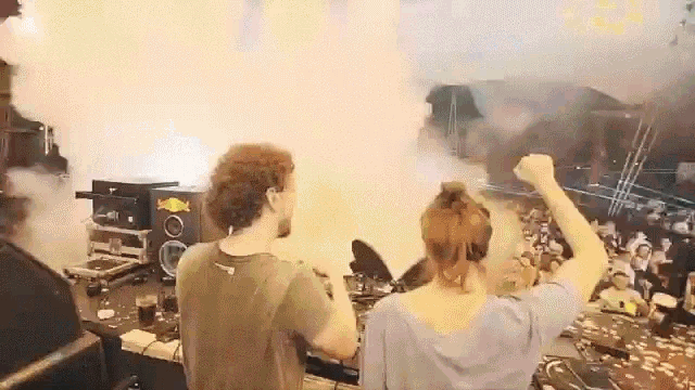 a man and a woman are playing music on a stage with smoke coming out of the speakers .