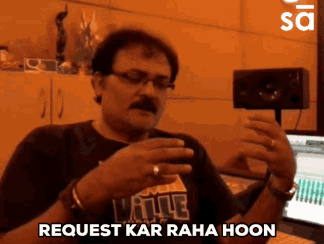 a man with a mustache and glasses is holding a cell phone and says " request kar raha hoon "