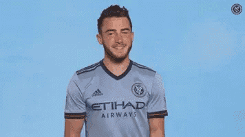 a man in a soccer jersey is clapping his hands in front of a blue background .