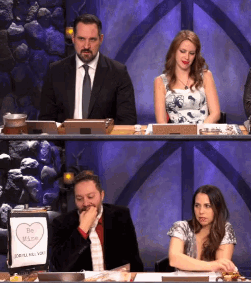a man and woman sit at a table with a sign that says be mine
