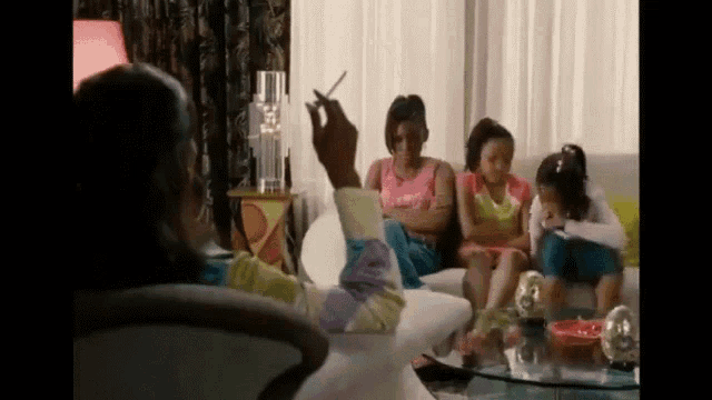 a woman is smoking a cigarette while sitting on a couch with three other women .