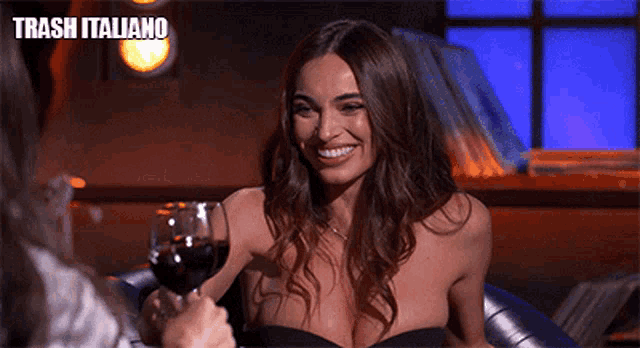 a woman in a black dress is holding a glass of wine in front of a trash italiano logo