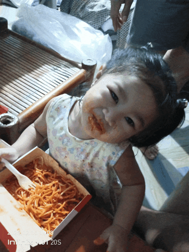 a little girl is eating spaghetti from a box with a fork