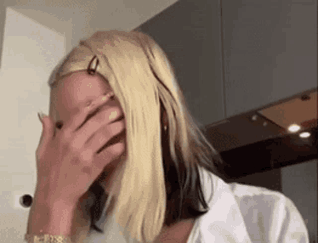 a woman is covering her face with her hand in a kitchen .
