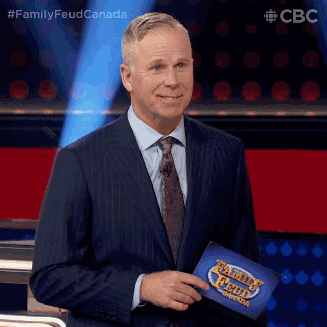 a man in a suit and tie holding a family feud canada sign