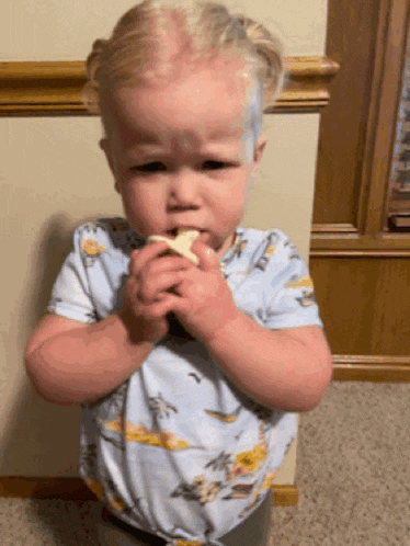 a little boy is eating a banana and has paint on his head .