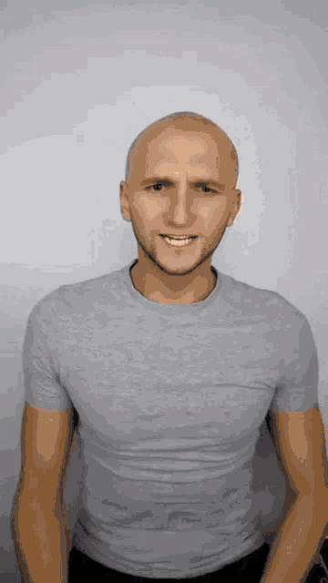 a bald man wearing a grey t-shirt is smiling .