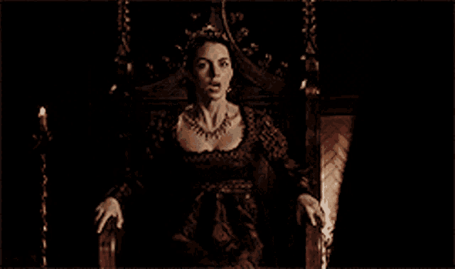 a woman in a red dress is sitting on a throne in a dark room .