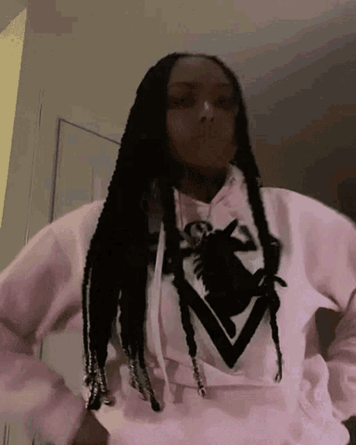 a woman with braids is wearing a pink hoodie with a black and white logo on it .