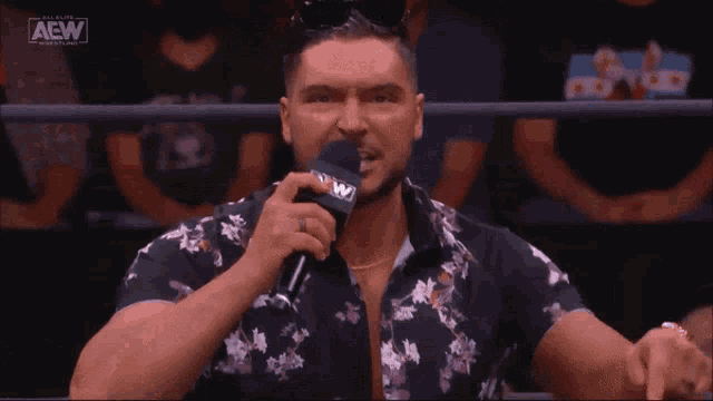 a man in a floral shirt is holding a microphone and saying i dress like a champ