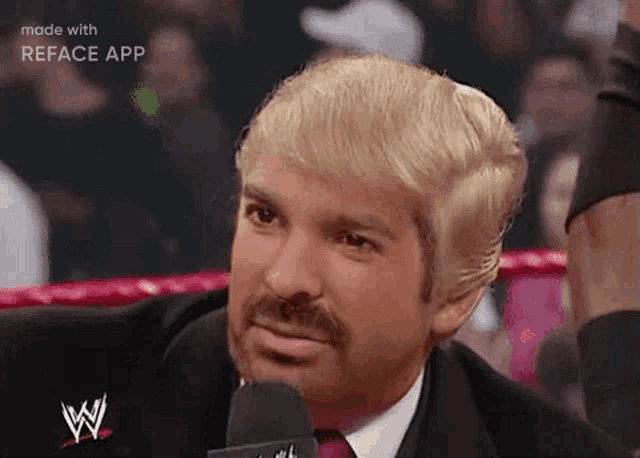 a man with blonde hair and a beard is talking into a microphone .