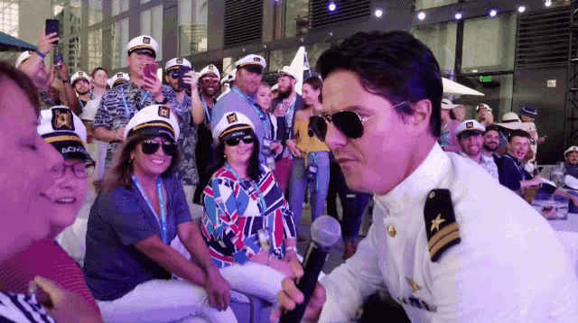 a man in a captain 's uniform is holding a microphone in front of a crowd of people