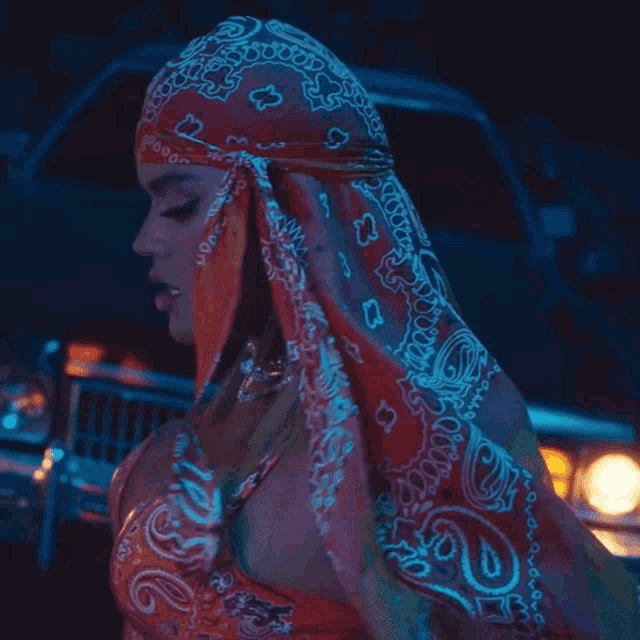 a woman wearing a red bandana covering her face stands in front of a car