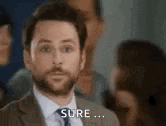 a man in a suit and tie is standing in front of a group of people and saying `` sure '' .