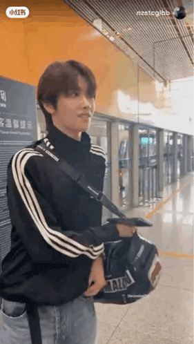 a young man is carrying a bag on his shoulder while standing in a train station .