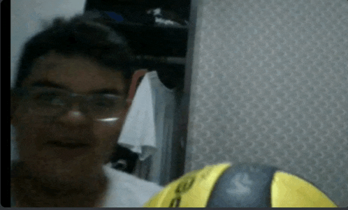 a man wearing glasses is holding a yellow ball with the letter s on the back