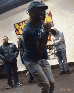 a man in a blue shirt and hat is dancing in a room with other men .