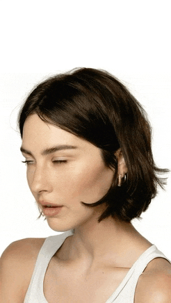 a woman with short brown hair is wearing a white tank top and hoop earrings