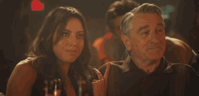 a man and a woman are sitting at a table and the woman is pointing