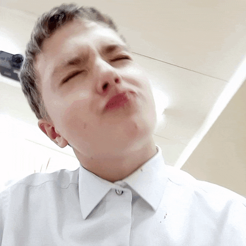 a young man in a white shirt is making a funny face with his eyes closed
