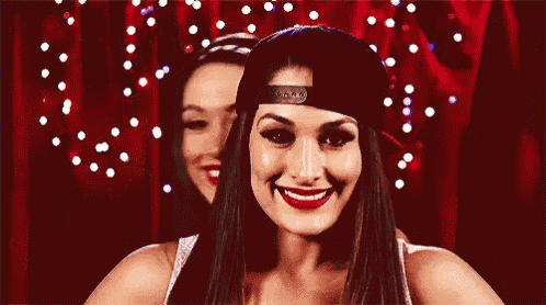 two women are smiling for the camera while wearing baseball caps .