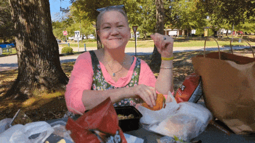 a woman sits at a picnic table with a bag of tortilla chips