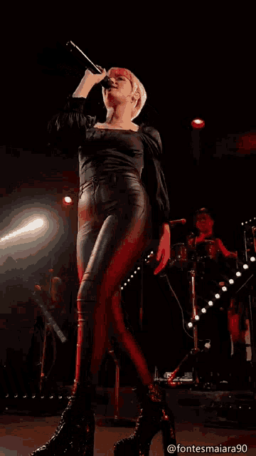 a woman is singing into a microphone on a stage with a man behind her