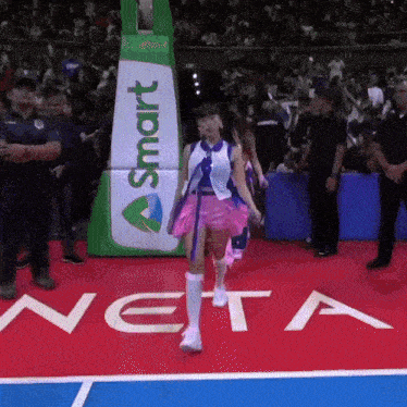 a girl in a pink skirt is walking on a basketball court with a smart sign in the background