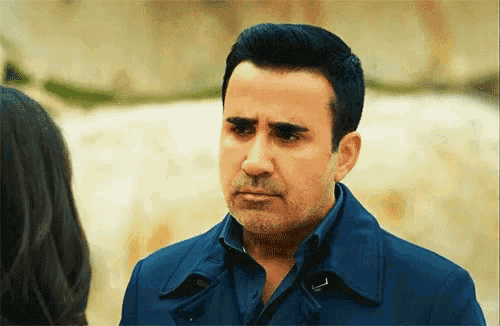 a man in a blue coat looks at a woman with a sad look on his face