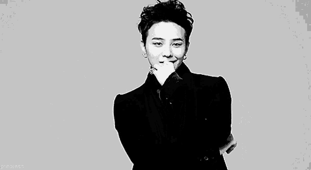 a black and white photo of a young man wearing a black suit and earrings .