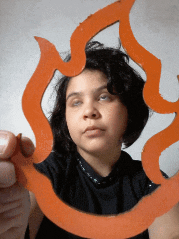 a woman in a black shirt is holding a piece of cardboard that looks like a flame
