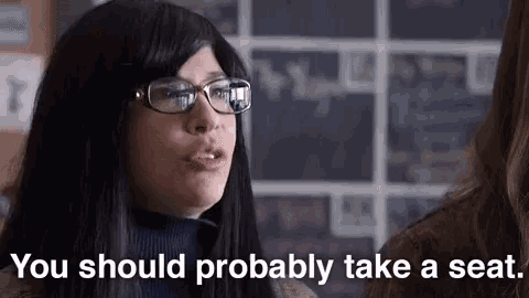 a woman wearing glasses is talking to another woman and says `` you should probably take a seat ''