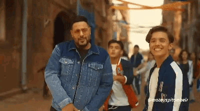 a man wearing a denim jacket is standing next to a boy wearing a jacket with the letter m on it