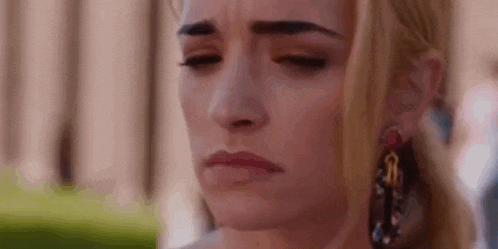 a close up of a woman 's face with a sad look on her face and earrings .