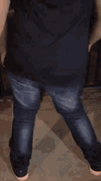 a man wearing a black shirt and blue jeans is standing on a tiled floor .