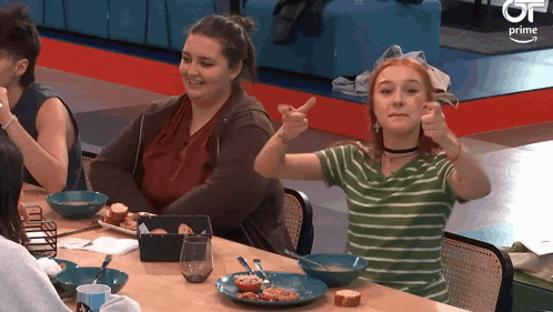 a woman giving a thumbs up while sitting at a table with plates of food