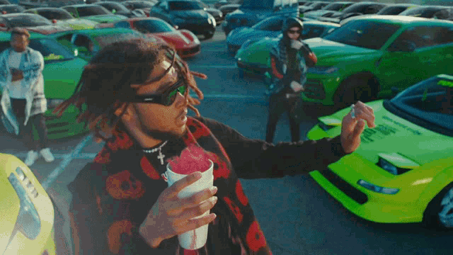 a man with dreadlocks is holding a cup of ice cream in front of a parking lot full of cars
