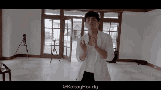 a man in a white shirt is dancing in an empty room with the hashtag kokoyhourly on the bottom