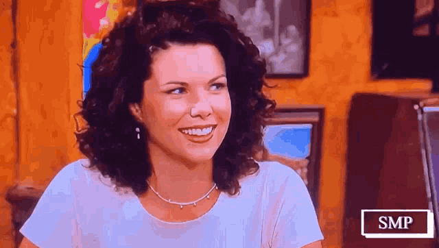 a woman with curly hair is smiling in front of a sign that says smp on it