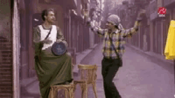 a man is sitting on a chair playing a drum while another man is standing next to him .