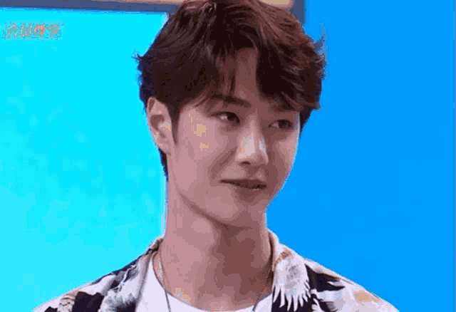 a young man with a necklace around his neck is standing in front of a blue wall .