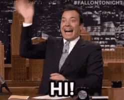 a man in a suit and tie is waving his hand and saying hi