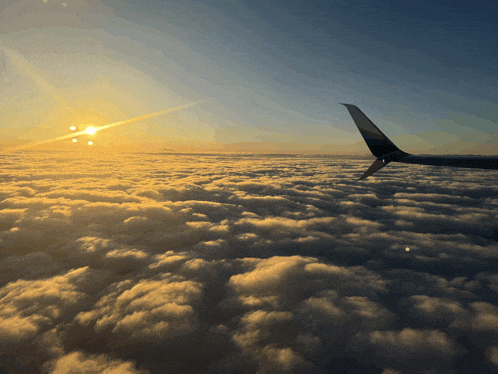 the wing of an airplane flying over the clouds at sunset