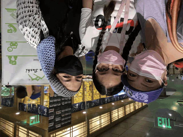 three people wearing face masks in front of a sign that says exit