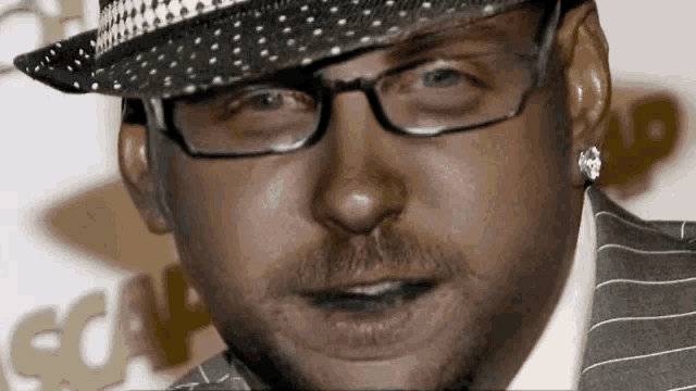 a man wearing glasses and a hat is standing in front of a sign that says " gq "