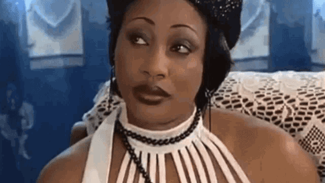 a woman wearing a striped dress and a necklace is sitting on a couch looking at the camera .