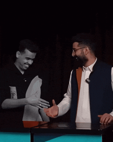 two men are shaking hands in a dark room and one has a sticker on his shirt that says ' x '