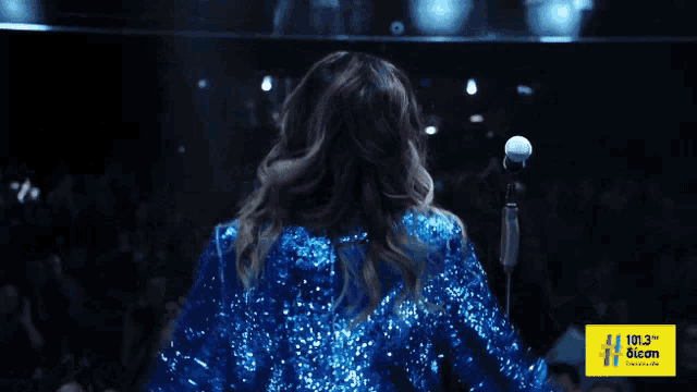 a woman in a blue sequined jacket is dancing in front of a yellow sign that says 101.3 fm