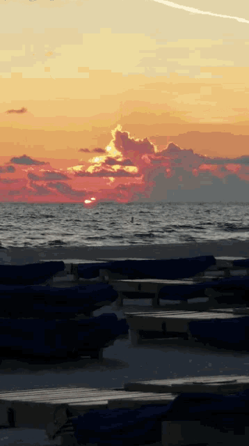 a sunset over a body of water with a few tables in the foreground